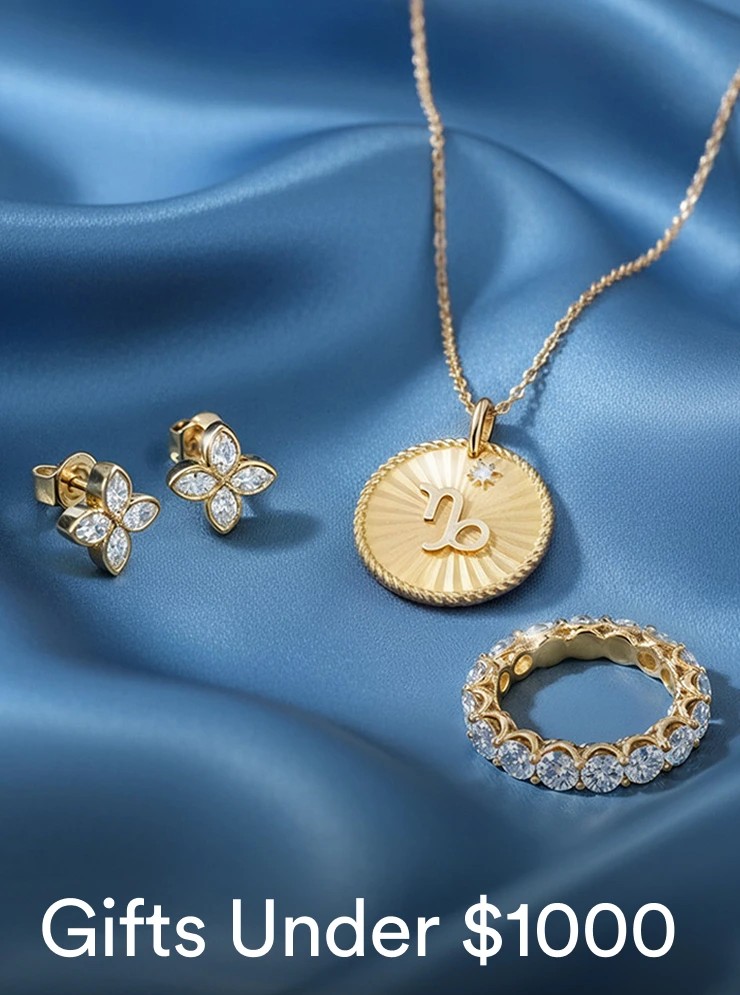 On a luxurious blue fabric, different bestselling under $1000 jewelry pieces are scattered with a text "Gifts under $1000"