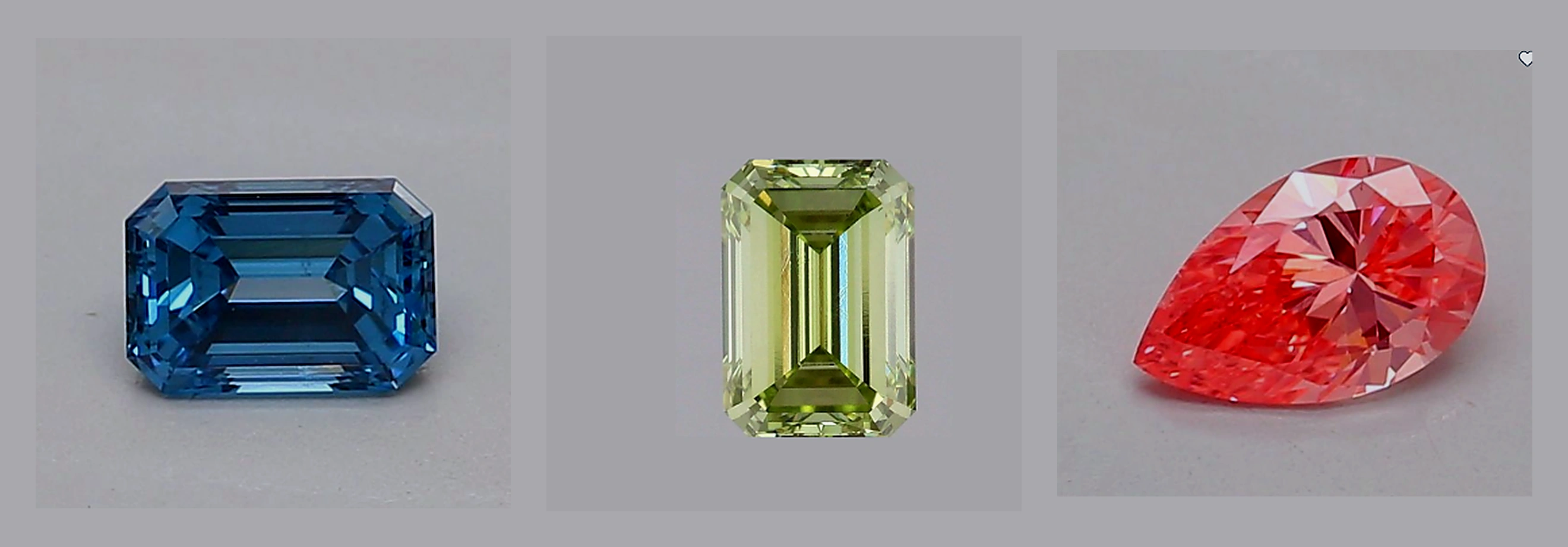 Three loose fancy color diamonds side by side on a neutral gray background: a blue emerald-cut, a green emerald-cut, and a pink pear-cut diamond.
